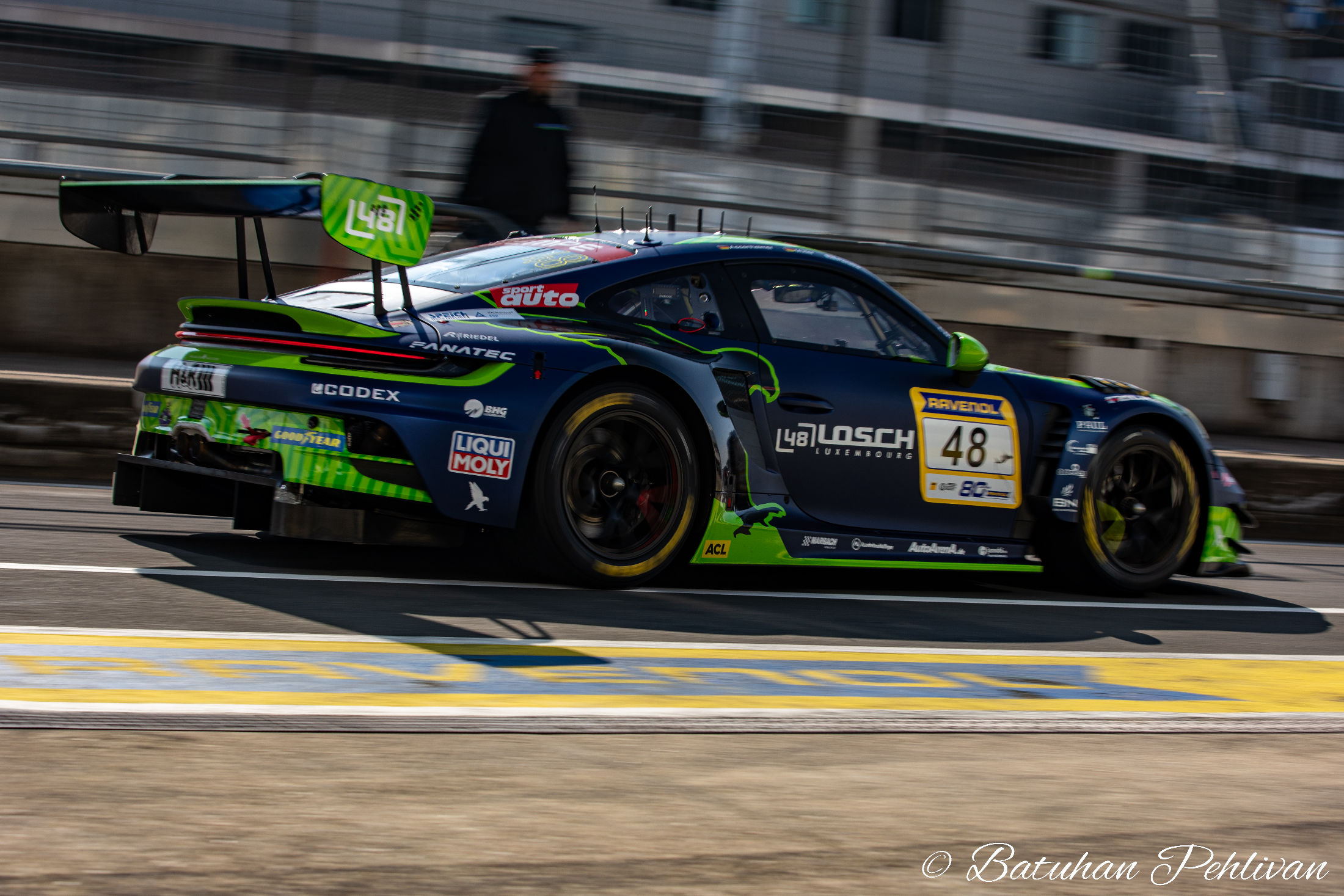 Green and black GT race car captured at speed on track during a motorsport event at the Nürburgring.